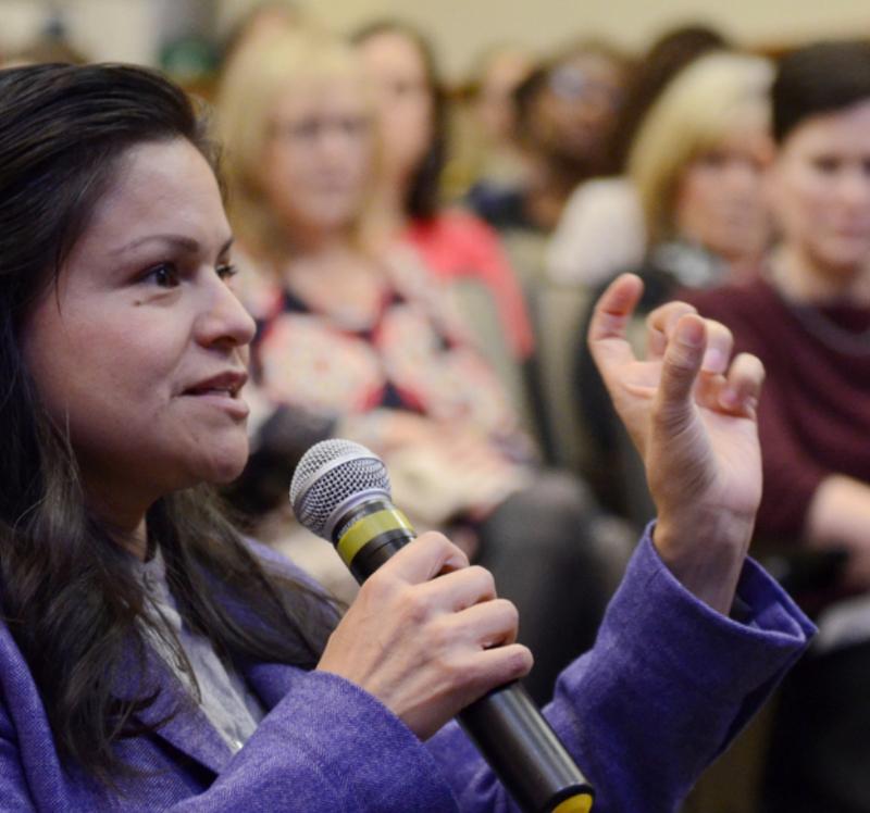 A woman asking a question into a microphone at a conference.