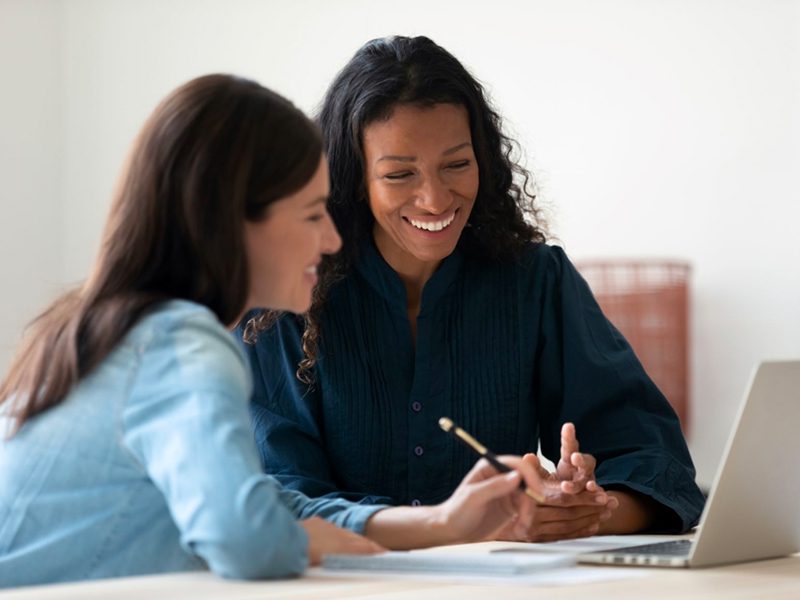 Two women smiling and talking as they look at a laptop.