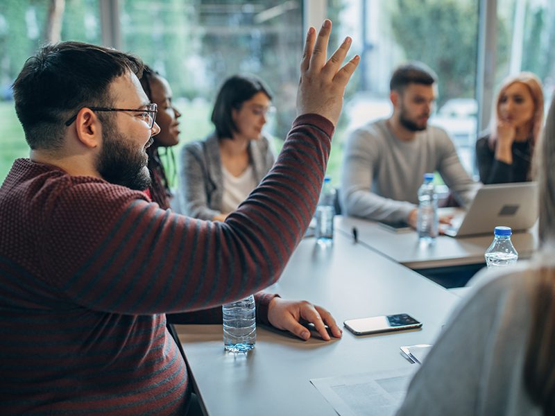 Man raises hand at a meeting.