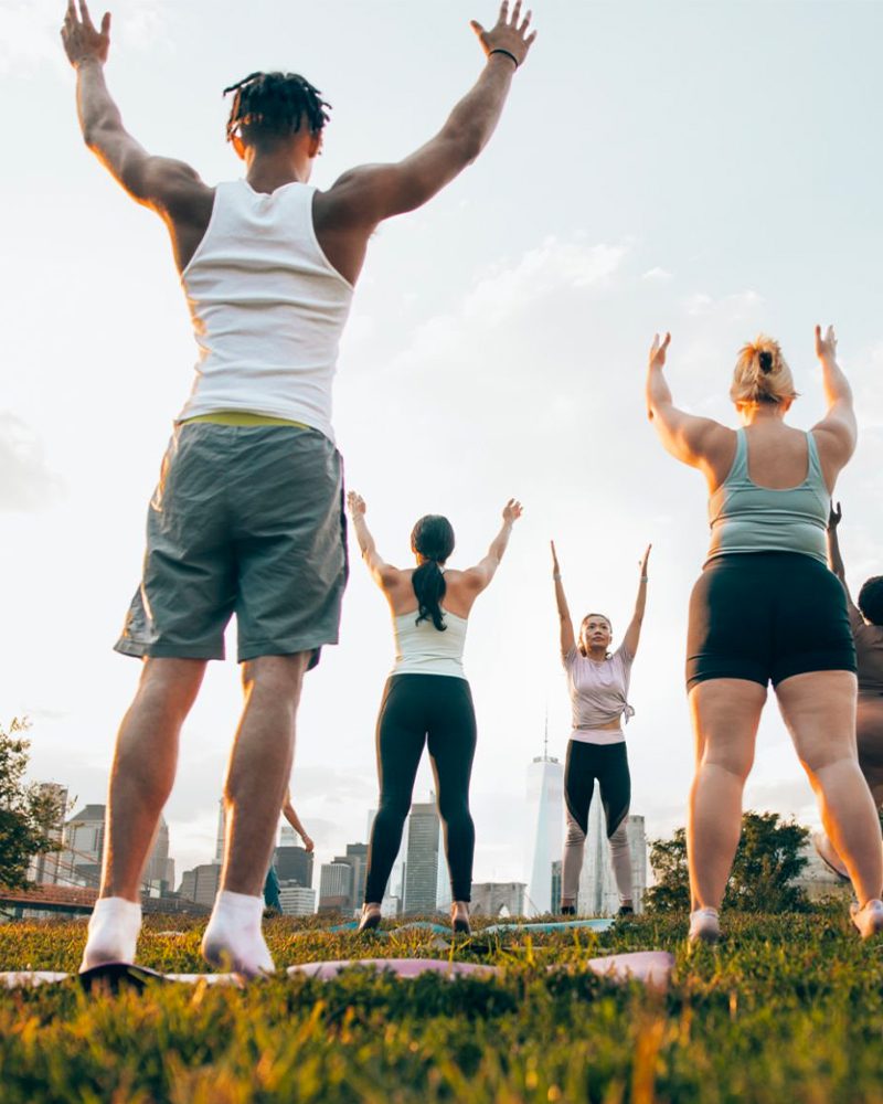 Instructor leads outdoor yoga at a park with city background at dawn